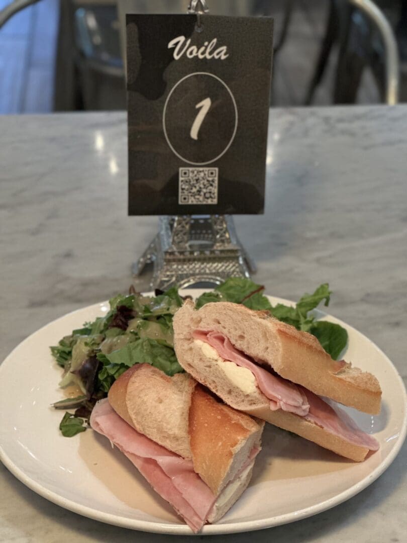 Ham sandwich with salad on white plate.